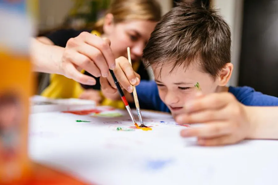 Teacher helping young boy to paint