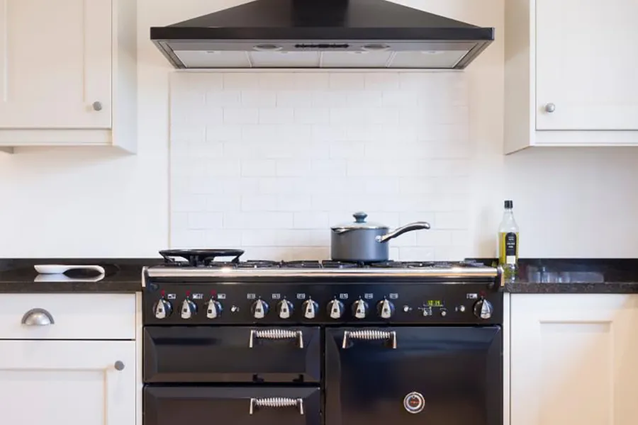 Close up of white kitchen with black worktop. Saucepan positioned on top of a black range cooker.