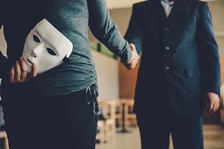 Two people shaking hands, one with a mask behind their back
