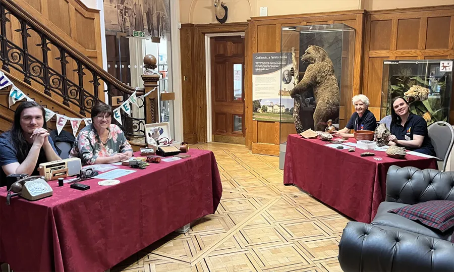 Museum of Chelmsford staff sat in the museum at two trestle tables with items in front of the them from exhibitions.